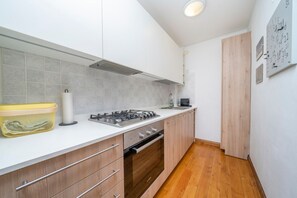 A modern kitchen with white cabinets, a gas stove, a built-in oven, and a wooden floor. - GuestHost - Charming studio in Tarvisio, ideal for 3 people, equipped with a balcony offering breathtaking views of the Alps. The accommodation is perfect for a romantic getaway or a nature adventure. Tarvisio is a paradise for winter sports enthusiasts  (Tarvisio)