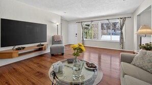 A living room with a flat-screen TV, a glass coffee table, a sofa, and a window with curtains. - St Paul Retreat:  Fireplace & Pet-Friendly (Saint Paul)