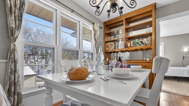 A dining area with a white table set for four, a loaf of bread, and a wooden bookshelf with various items. - St Paul Retreat:  Fireplace & Pet-Friendly (Saint Paul)
