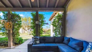 A covered patio with a black wicker sofa, a glass coffee table, and a patterned rug. - Heritage Hideaway | 2BR Legacy Villa (La Quinta)