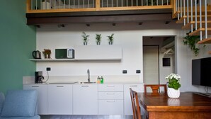 A modern kitchen with white cabinets, a microwave, and a coffee maker. There is a dining table with chairs and a small plant on it. - Loft Trevisan • Elegant loft with private garage (Bra)