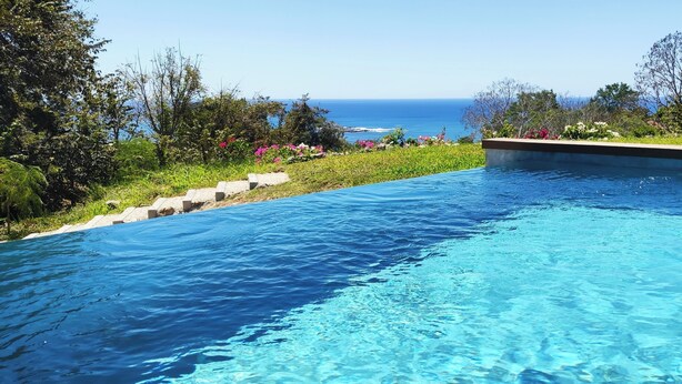Una piscina azul cristalina con vista al océano y un jardín ajardinado.