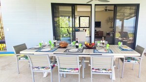 Un área de comedor al aire libre con una mesa preparada para cuatro personas, rodeada de sillas con cojines de colores.