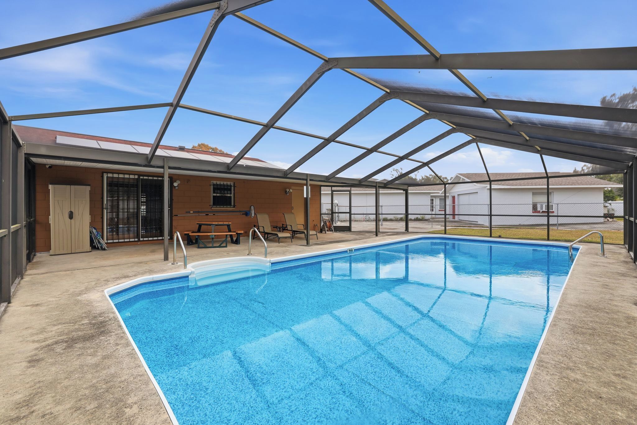 A covered swimming pool with a metal roof, adjacent to a building with a door and windows.