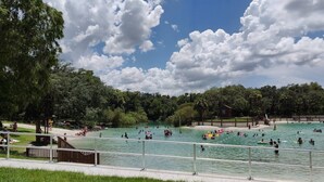 Une piscine publique dotée de plusieurs couloirs, entourée d’une végétation luxuriante et offrant une vue sur un ciel dégagé.