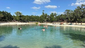 Une piscine aux eaux cristallines, entourée d’arbres, et une plage de sable fin.