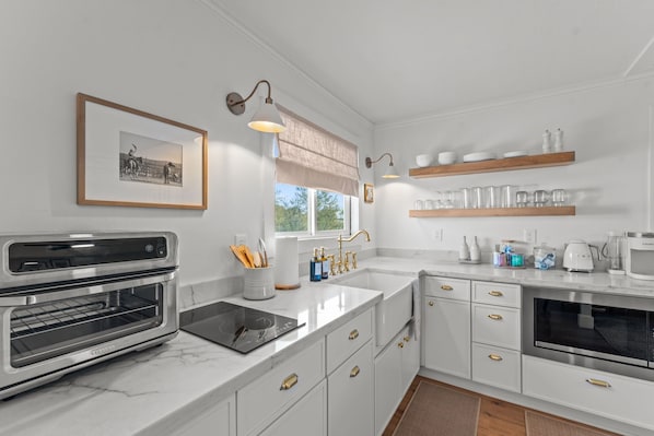 A modern kitchen with white cabinetry, a built-in oven, a microwave, and a window with a view of the outdoors.