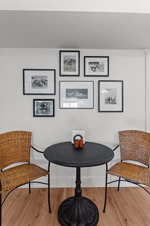 Una habitació amb una taula rodona, dues cadires de vimetes i sis fotografies emmarcades a la paret.