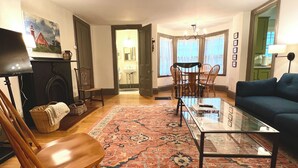 Een woonkamer met een houten stoel, een glazen salontafel, een blauwe bank, een kamerkleed met een patroon en een open haard.