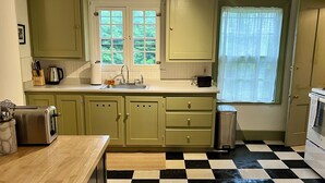 Een keuken met een zwart-wit geruite vloer, houten kastjes, een spoelbak en een raam met uitzicht op groen.