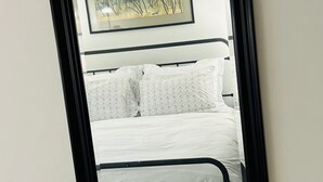 Een spiegel toont een bed met hoofdeinde, kussens en een ingelijste foto aan de muur.
