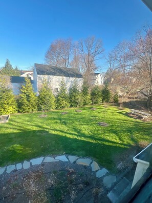 A stone pathway leading to a grassy yard with trees and a building in the background.