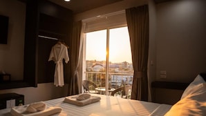 Habitación de hotel con cama, ventana con cortinas, mesa con sillas y una bata colgada en la pared.