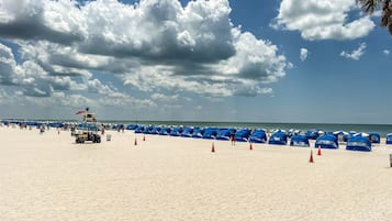 A beach with numerous blue umbrellas and a lifeguard tower.