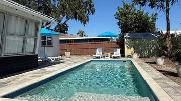 A rectangular swimming pool with a tiled deck, surrounded by lounge chairs and umbrellas.