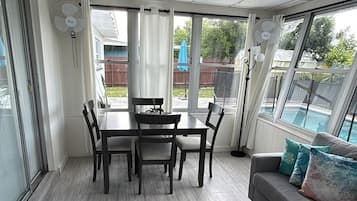 A sunroom with a dining table and chairs, a gray sofa, and a view of a swimming pool.