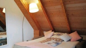 Um quarto de sótão aconchegante com teto de madeira, uma cama com cobertor rosa e um tapete fofo.