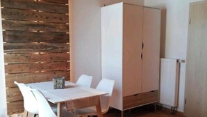 Quarto com teto de madeira, uma mesa branca com cadeiras, guarda-roupa e radiador.