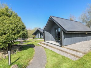 A modern building with a sloped roof, a pathway leading to the entrance, and a small tree in the foreground. - Glamping Pod 1 - Gower (Swansea)
