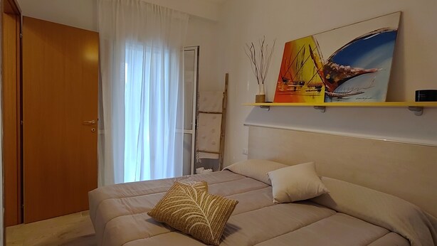 A bedroom with a bed, a painting, a shelf, and a door.