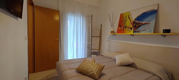 A bedroom with a bed, a painting, a shelf, and a door.