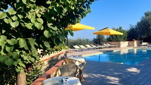A swimming pool with lounge chairs and yellow umbrellas, surrounded by greenery.