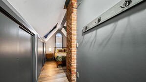 A narrow hallway with wooden flooring, a brick column, and a bed with a patterned bedspread. - Spacious 5BR Retreat - Duplex close to Attitash (Bartlett)