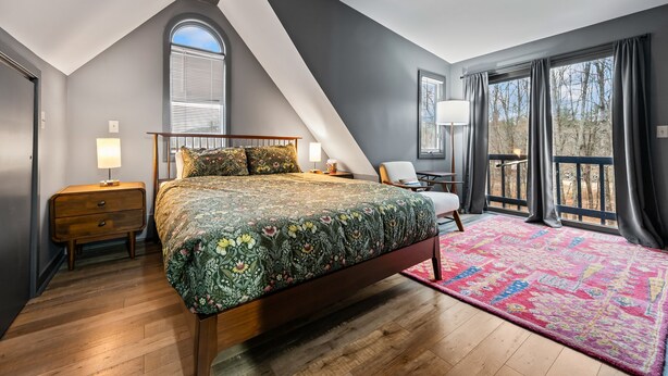 A bedroom with a large bed, a wooden nightstand, a desk, and a chair. There are large windows with curtains and a view of trees. - Spacious 5BR Retreat - Duplex close to Attitash (Bartlett)
