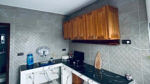Eine Küche mit grauen Fliesen, Holzschränken, einer schwarzen Arbeitsplatte, einem Spülbecken und einer Kaffeemaschine.