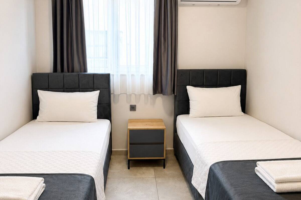 Une chambre d’hôtel avec deux lits, une petite table de chevet en bois, une fenêtre avec des rideaux et un appareil de climatisation.