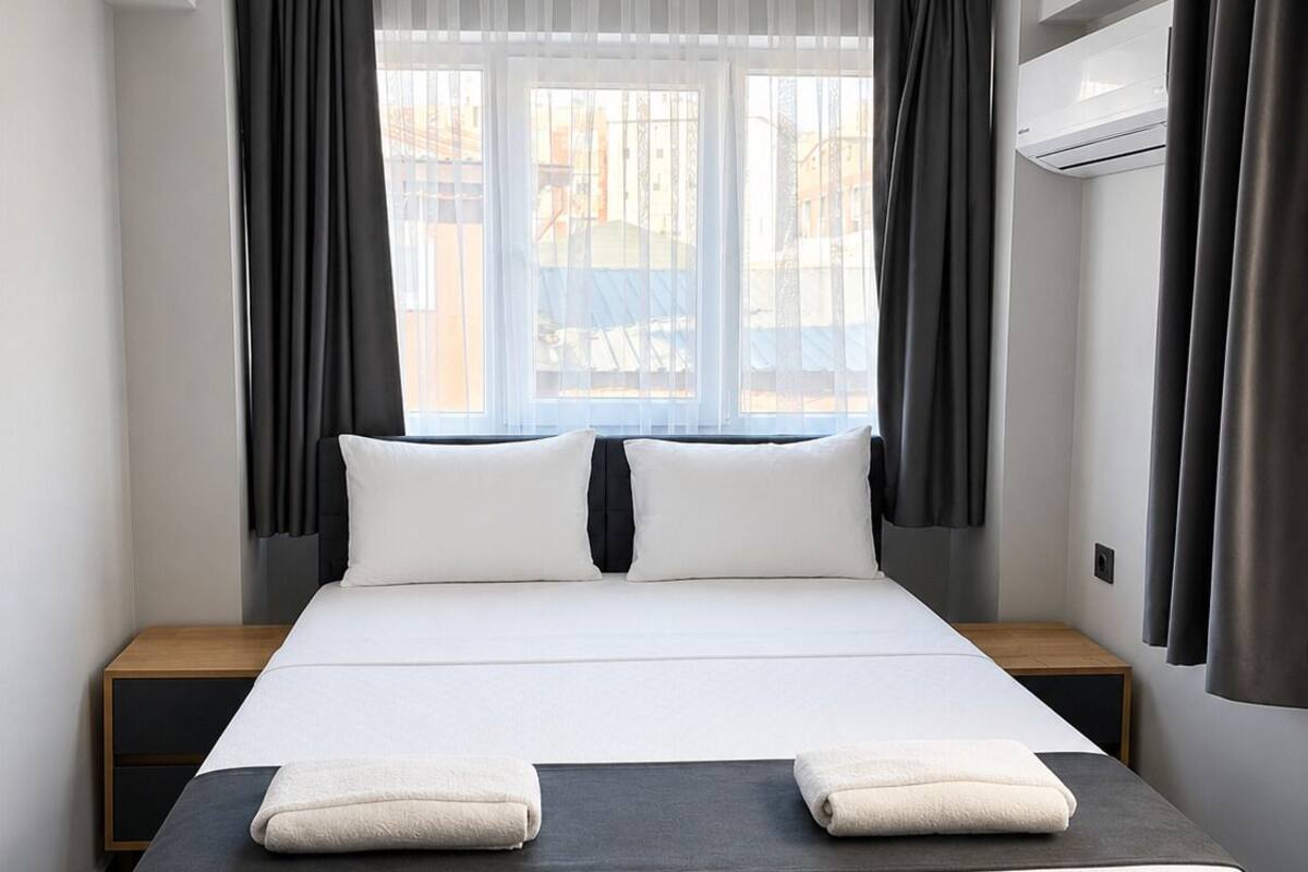 Une chambre d’hôtel avec un grand lit, deux tables de chevet, un bureau et une fenêtre avec des rideaux.