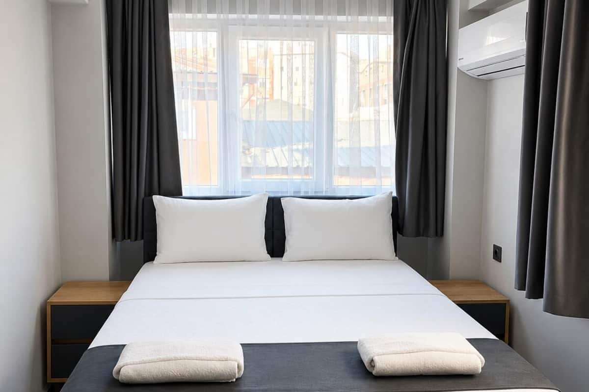 A hotel room with a large bed, two bedside tables, a desk, and a window with curtains.