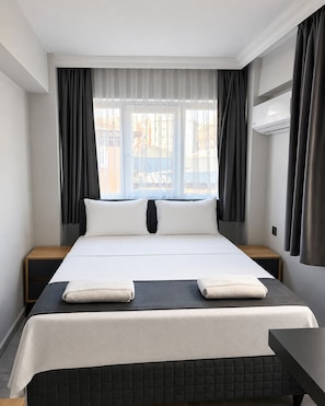 A hotel room with a large bed, two bedside tables, a desk, and a window with curtains. - Kaya Hotel (Antalya)