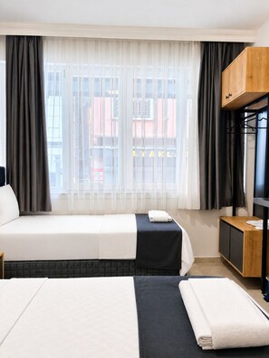 Ein Hotelzimmer mit zwei Betten, einem Holzschrank und Blick auf Gebäude durch leichte Vorhänge.