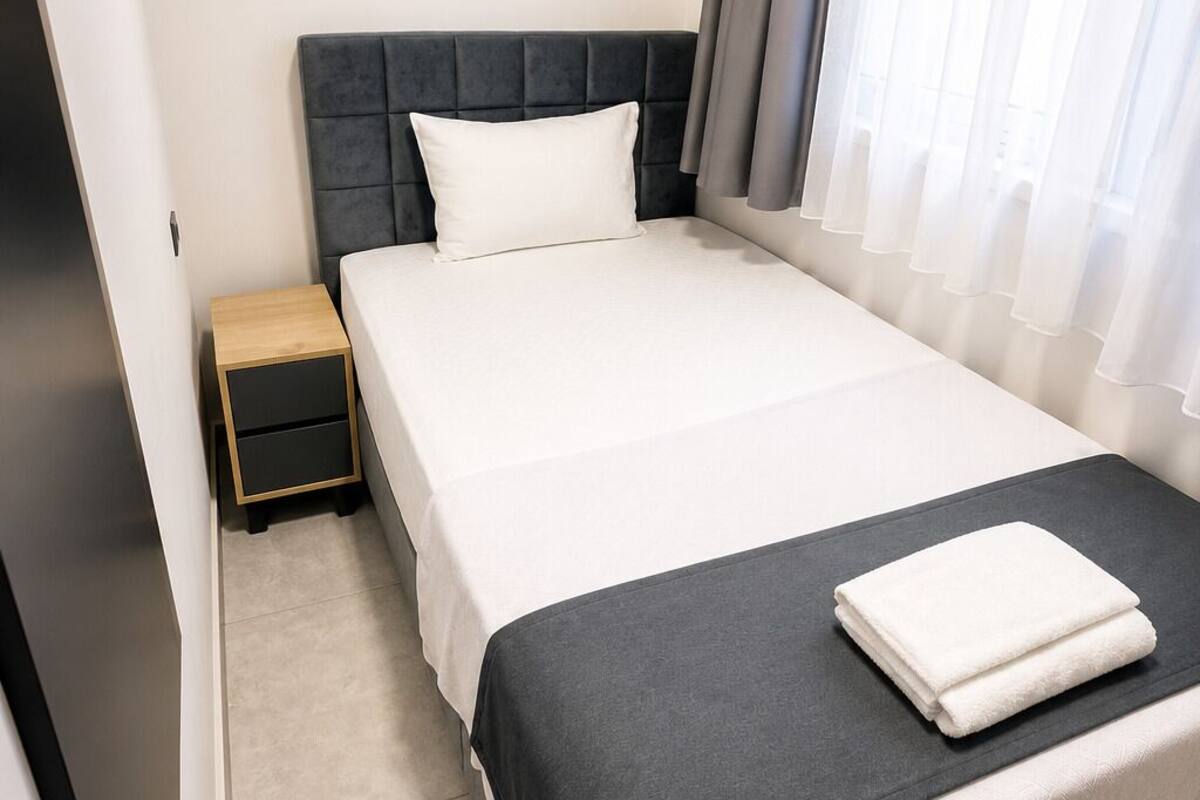 Une chambre d’hôtel équipée d’un lit, d’une table de chevet, d’un appareil de climatisation et d’une fenêtre avec des rideaux.