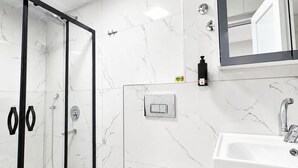 A modern bathroom with a glass shower enclosure, a white toilet, a sink with a mirror, and a marble-patterned wall.