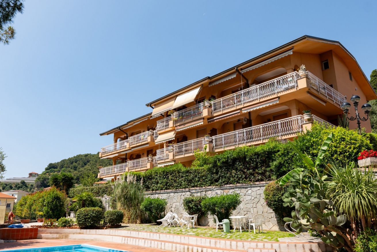 Ein mehrstöckiges Hotel mit Balkonen, einem Schwimmbad und üppiger Bepflanzung.