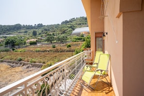 A balcony with a metal railing, two yellow lounge chairs, and a view of a green landscape with trees and a building in the distance. - The apartment is located in an area of ​​Bordighera surrounded by greenery, the perfect solution for a relaxing holiday, with all the main comforts!The private parking in the garage, the shared outdoor swimming pool, the large covered terrace with ou (Bordighera)