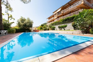 A swimming pool with a tiled deck, surrounded by greenery and a multi-story building with balconies. - The apartment is located in an area of ​​Bordighera surrounded by greenery, the perfect solution for a relaxing holiday, with all the main comforts!The private parking in the garage, the shared outdoor swimming pool, the large covered terrace with ou (Bordighera)