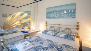 Un dormitorio con cama, un espejo grande, un cuadro de veleros y un adorno de pared.