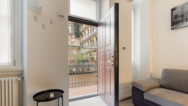 A room with a sliding glass door leading to a balcony, a radiator, a small table with a phone, and a sofa. - GuestHost - Cozy and quiet apartment in Milan! (Milano)