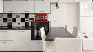 A modern kitchen with white cabinets, a red microwave, a black oven, and a dining table with chairs. - GuestHost - Cozy and quiet apartment in Milan! (Milano)