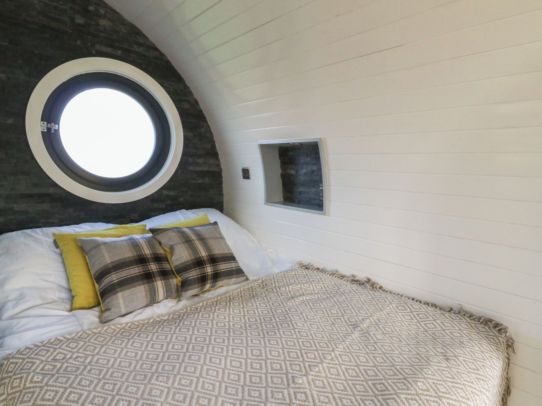 A bedroom with a round skylight, a bed with patterned bedding, and a small window.