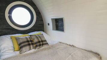 Un dormitorio con un tragaluz circular, una cama con ropa de cama estampada y una ventana pequeña.