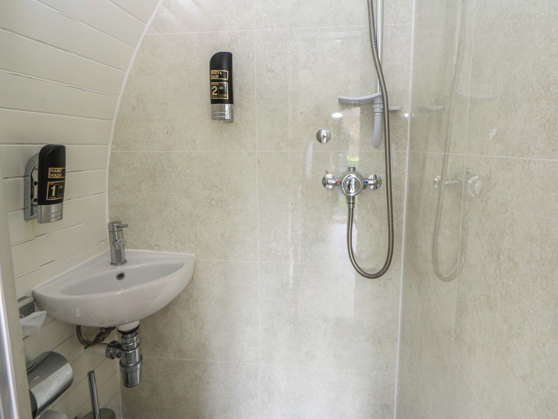 A bathroom with a sink, hand wash station, and shower.