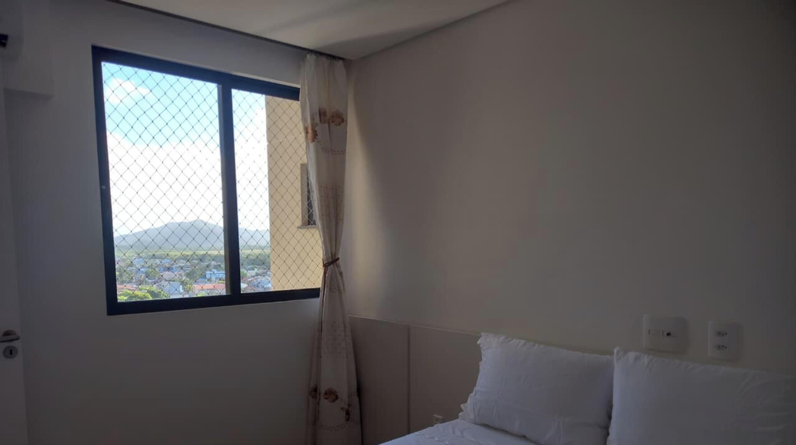 A bedroom with a bed, a window with a view of a cityscape, and a door.