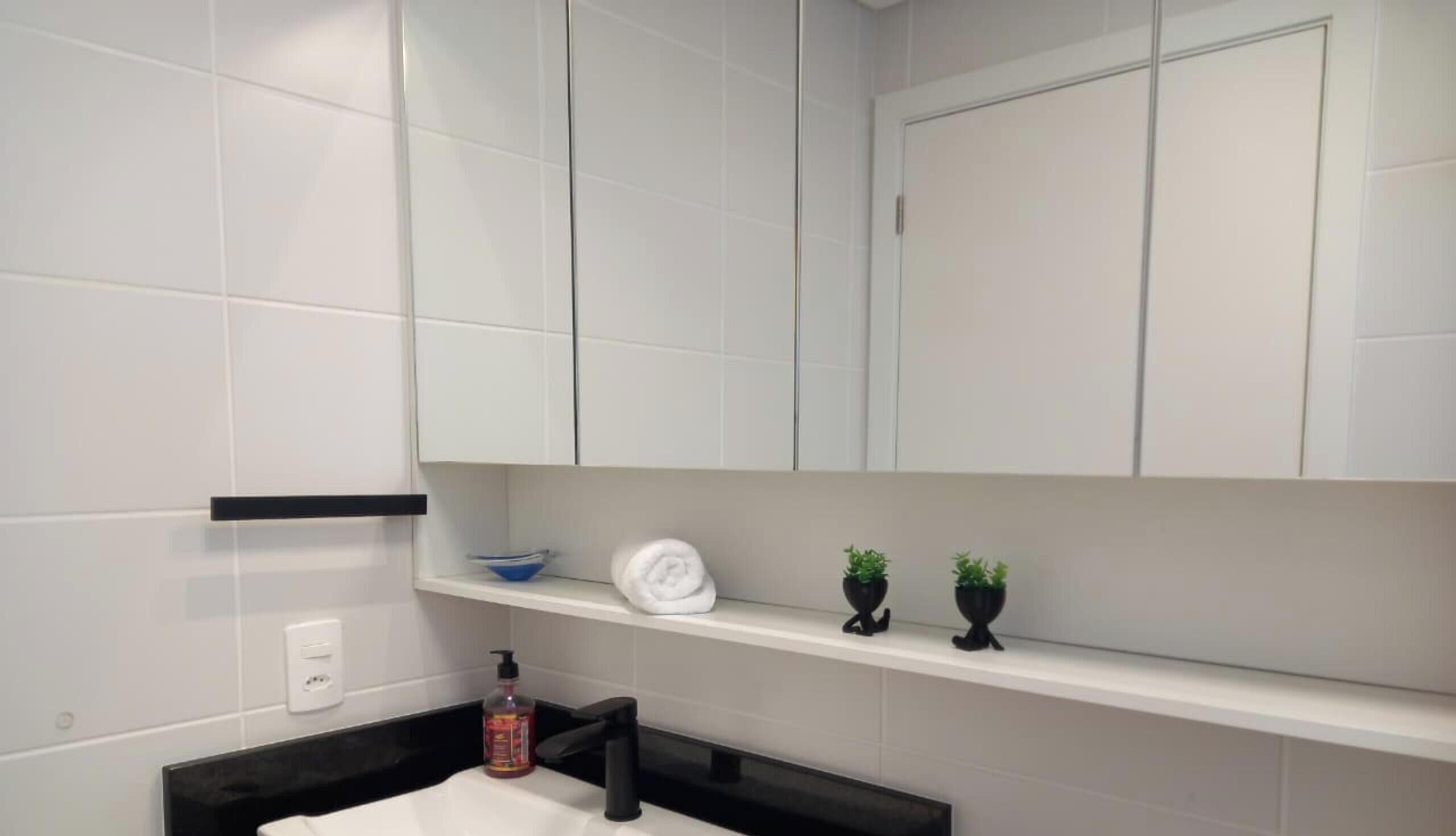 A modern bathroom with white tiles, a black countertop, a white towel, a blue bowl, and two small potted plants.