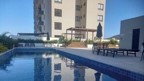 A swimming pool with tiled edges, surrounded by outdoor seating and a pergola. - Skyline Confort Club - Araucaria - Penha/sc (Penha)