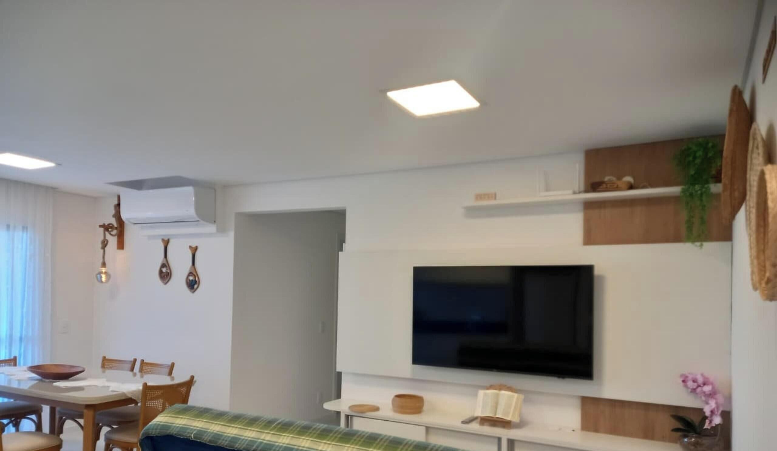 A modern living room with a flat-screen TV mounted on the wall, a dining area with a table and chairs, and a cozy seating area with a sofa.