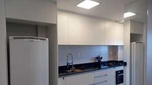 A modern kitchen with white cabinets, a black countertop, a built-in stove, and a refrigerator. - Skyline Confort Club - Araucaria - Penha/sc (Penha)